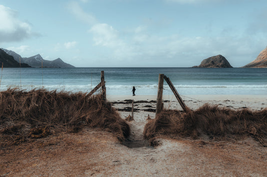 Lone figure walking on Haukland Beach with snow-covered mountains, Lofoten Norway