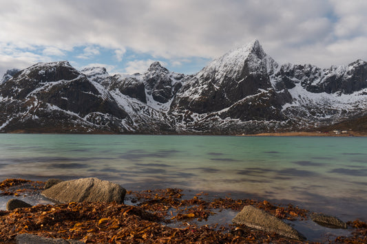 Mountain peak reflected in calm fjord water under overcast sky, Lofoten Norway