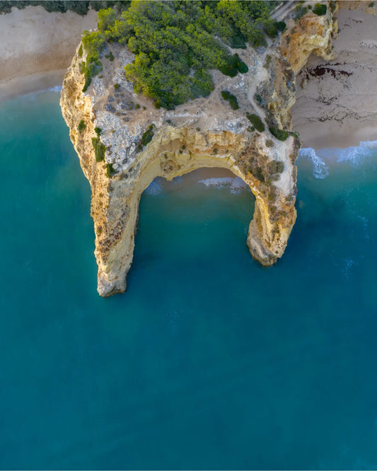 Top-down aerial view of rock arch and turquoise water near Praia da Coelha, Algarve, Portugal