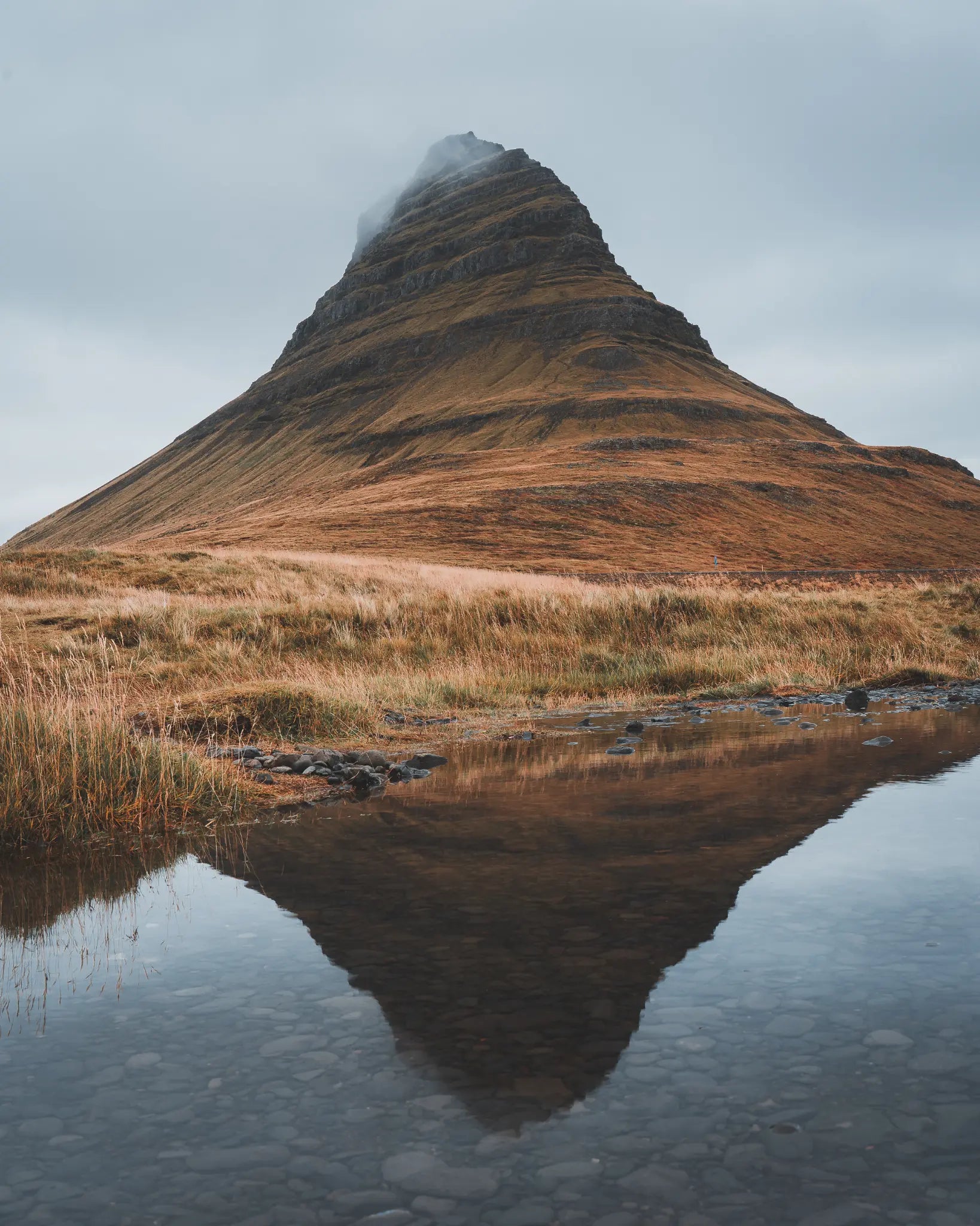 Kirkjufell mountain with autumn tundra and reflection pool under cloudy sky, Iceland