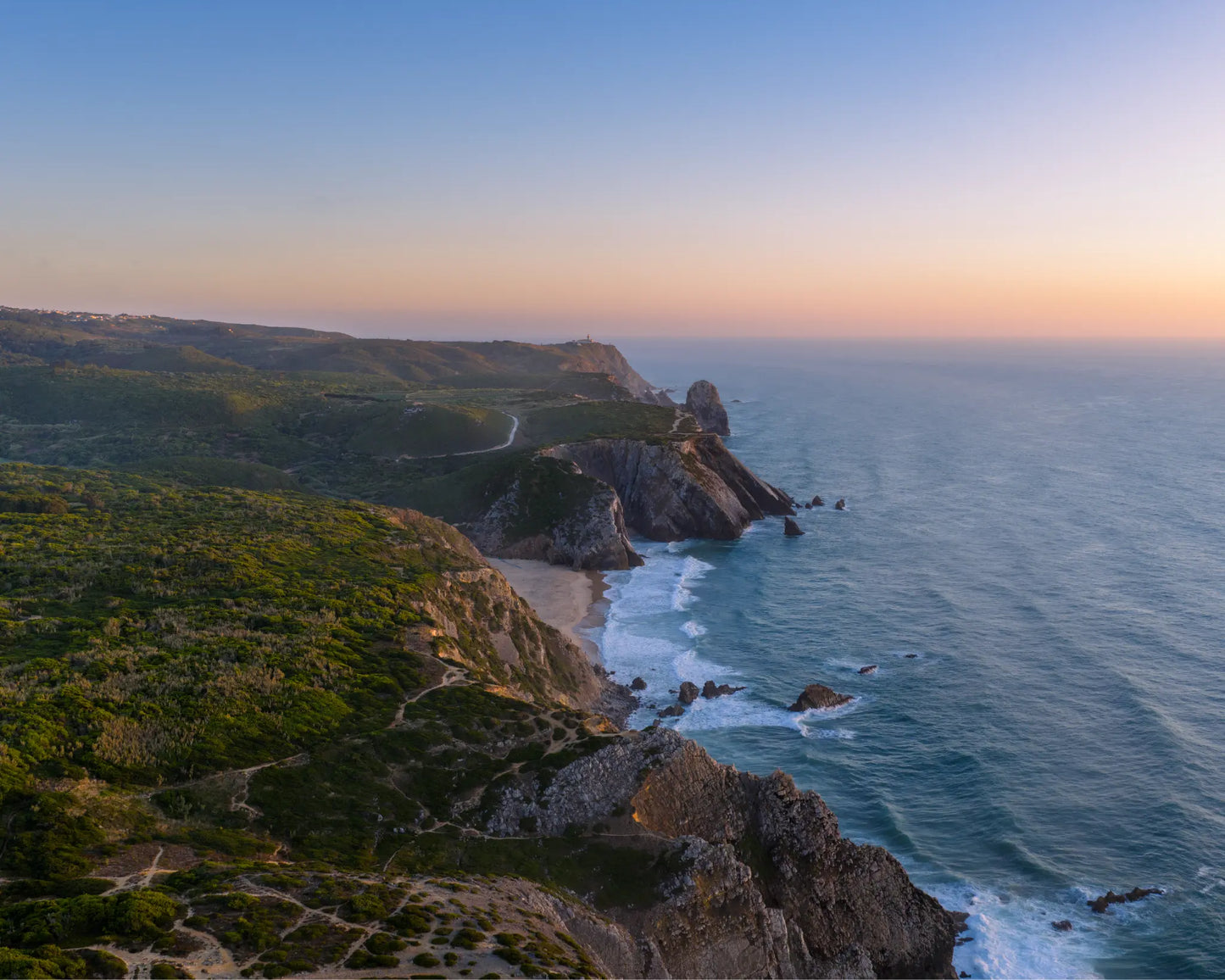 Aerial view of Praia da Adraga coastline at sunset with rock stacks, Sintra, Portugal